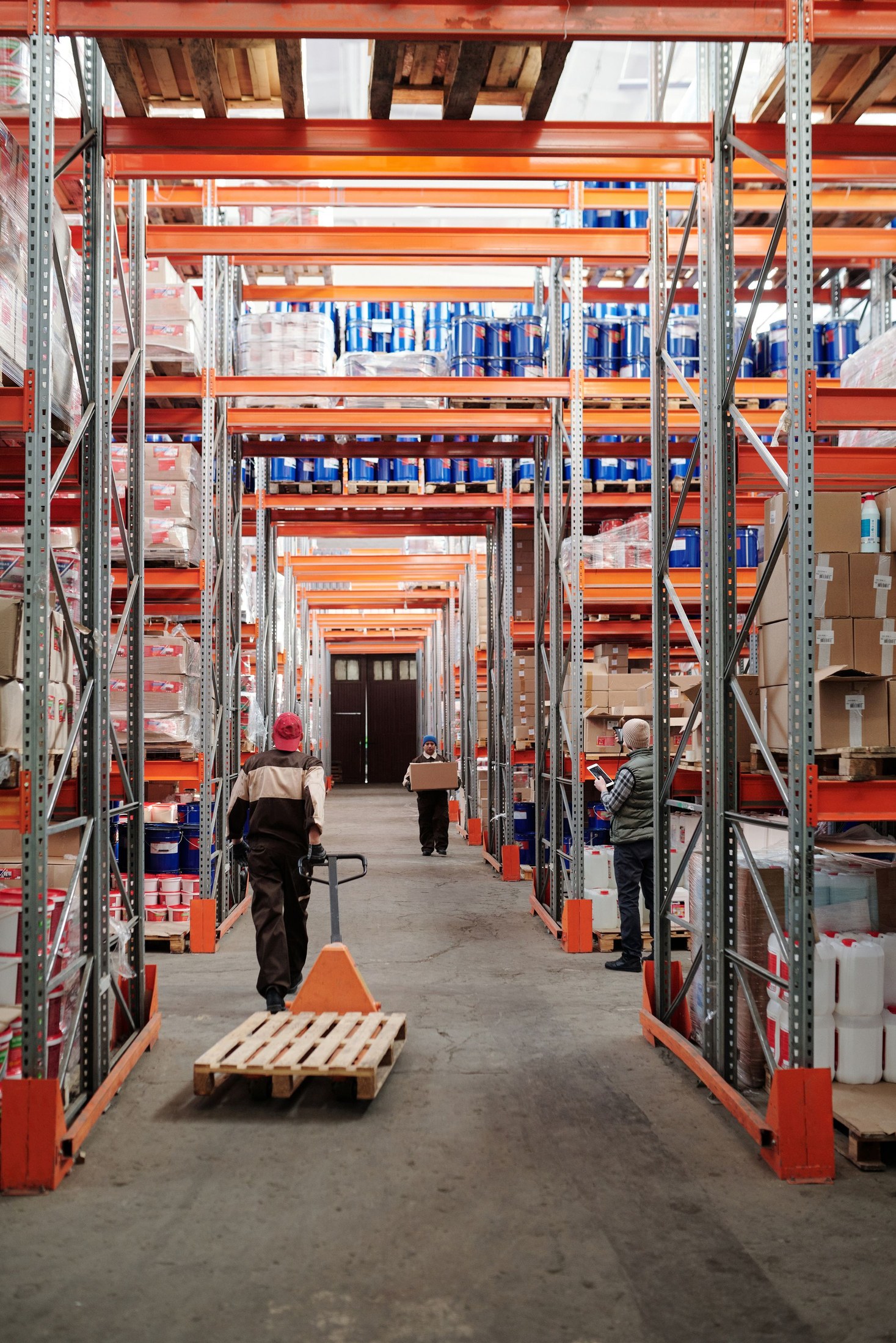 Warehouse worker pulling a wooden pallet with an orange pallet jack